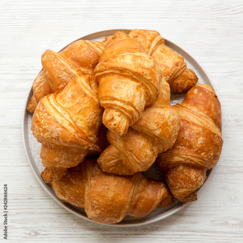 Freshly baked golden croissants on grey round plate on white wooden background, top view. From above, overhead, flat lay.