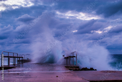 waves from a tropical storm crash down on this concrete dock. The volitile ocean was shot at sunset which is hard to see through the cloudy sky. Shot in Grand Cayman Caribbean