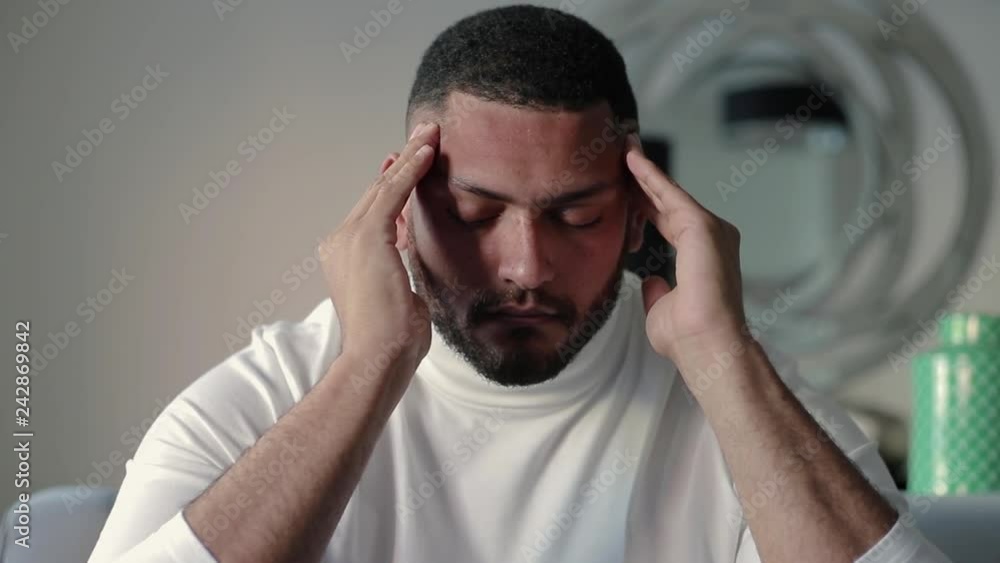 Tired mix raced guy suffering from headache. Young Latin man massaging temples and touching forehead with closed eyes. Head ache concept Tired mix raced guy suffering from headache. Young Latin man massaging temples and touching forehead with closed eyes. Head ache concept