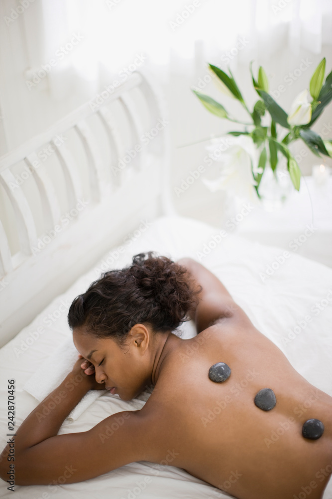 Young woman lying in bed on her stomach with healing stones on her back inside her bedroom. Young woman lying in bed on her stomach with healing stones on her back inside her bedroom.