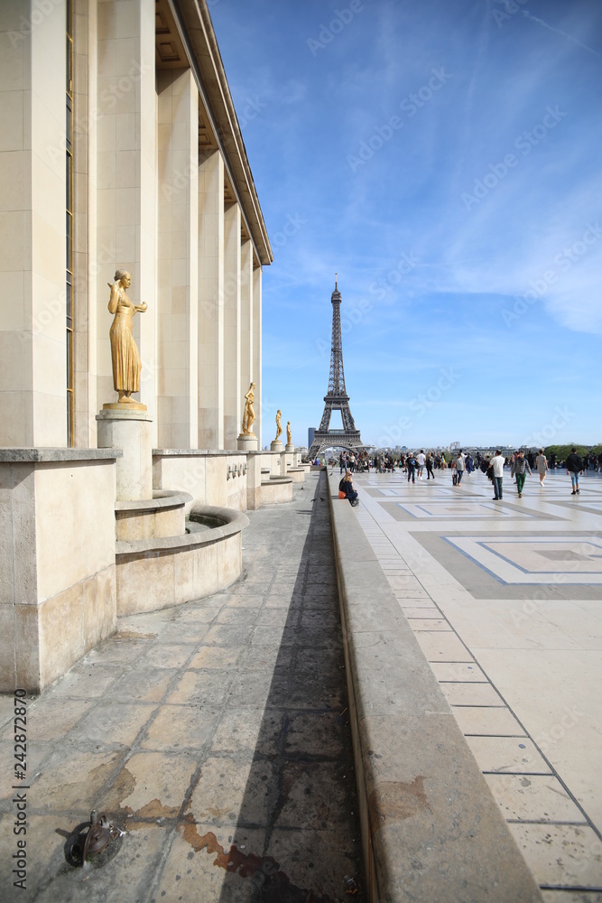 Tourists walk around the building with golden women and the Eiffel Tower is clearly visible