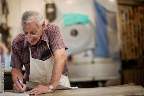Senior man writes on piece of paper at his place of work.