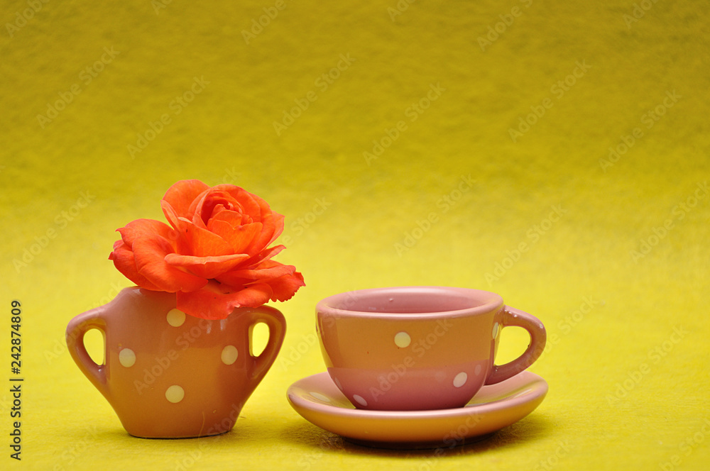A teacup with an orange rose on a yellow background A teacup with an orange rose on a yellow background