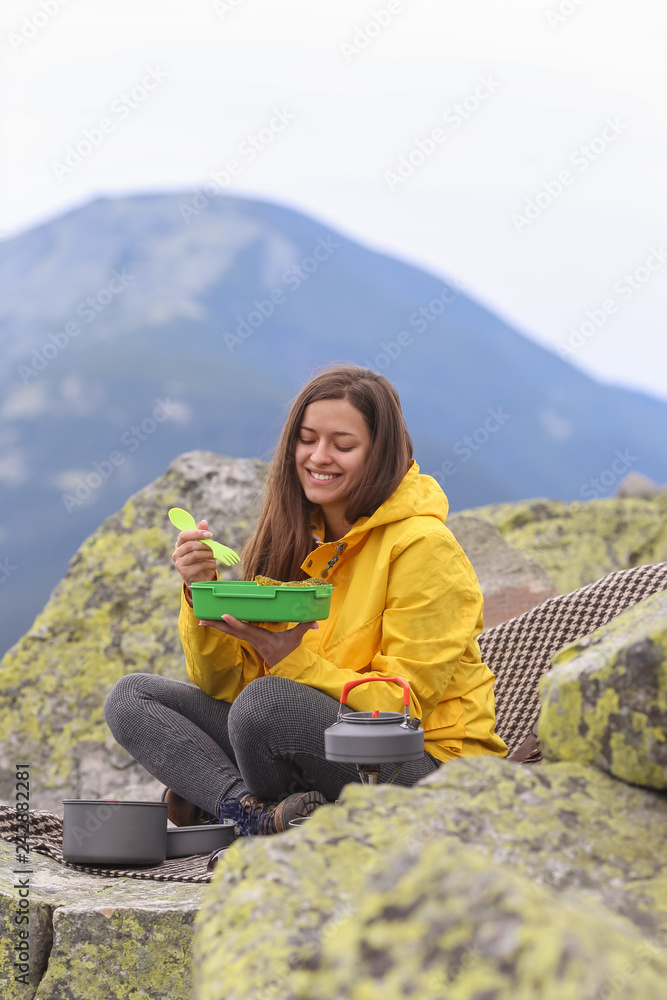 Fototapeta premium Young woman in yellow jacket have a picnic on top of the mountain. 
