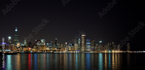 Long-exposure photo of downtown Chicago at night. The light of the stars can be see in the clear sky above  and the reflection of the city lights is in the lake in the foreground.