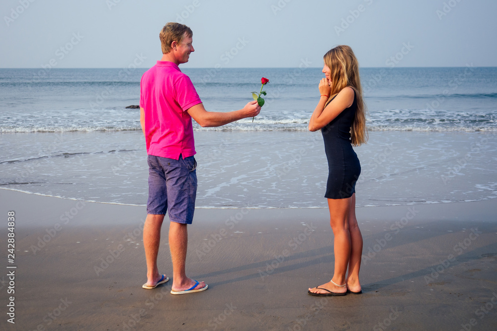 Fototapeta premium Valentine's Day February 14th a man gives a woman a rose standing on a beach by the sea summer morning