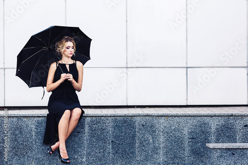 gorgeous woman with an umbrella sits on the parapet and waits.