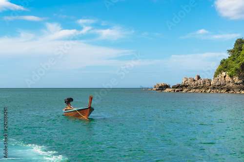 traditional Thai boat is anchored near a small rocky island in a calm sea on a sunny day