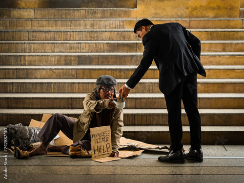 Fotografie A businessman gives smartphone to a homeless man sitting on a ladder