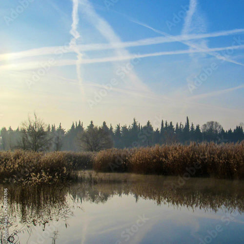 Winter lake landscape in early winter morning with blue sky and plane tracks reflected in water