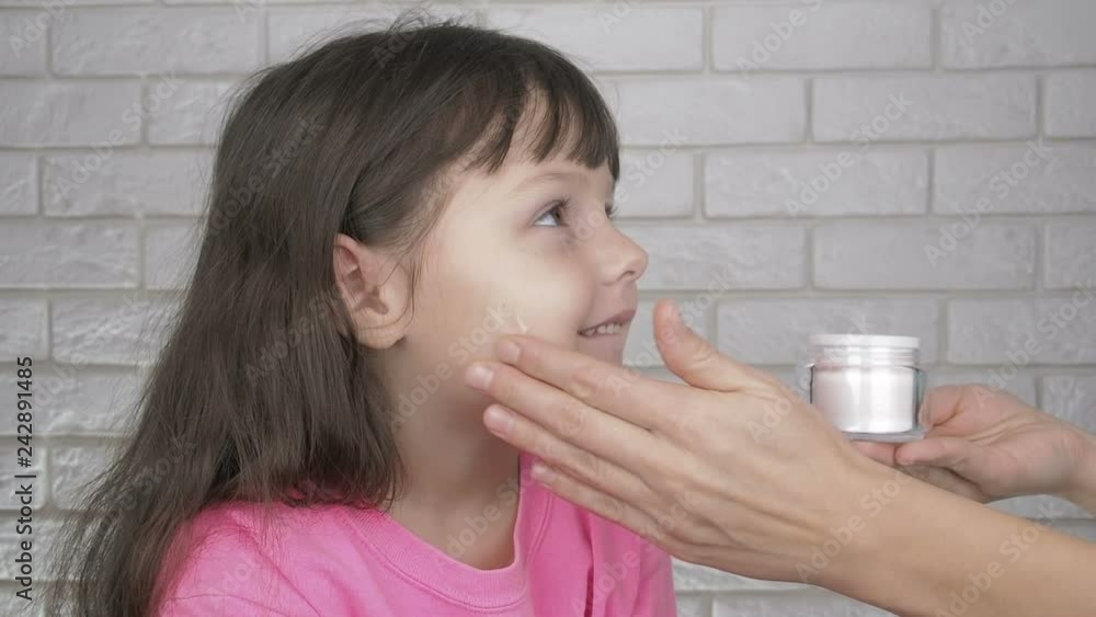 Parent moisturazes daughters skin. A little girl is smeared with cream on her face. Parent moisturazes daughters skin. A little girl is smeared with cream on her face.