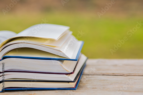 Pile of closed book with open book outdoors on wooden background