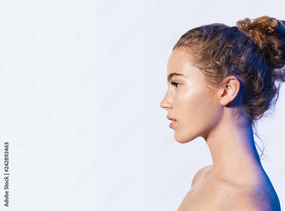 Portrait of young beautiful model with brown curly hair and shiny clean face posing with bare shoulders on white background. Perfect skin and wellness concept