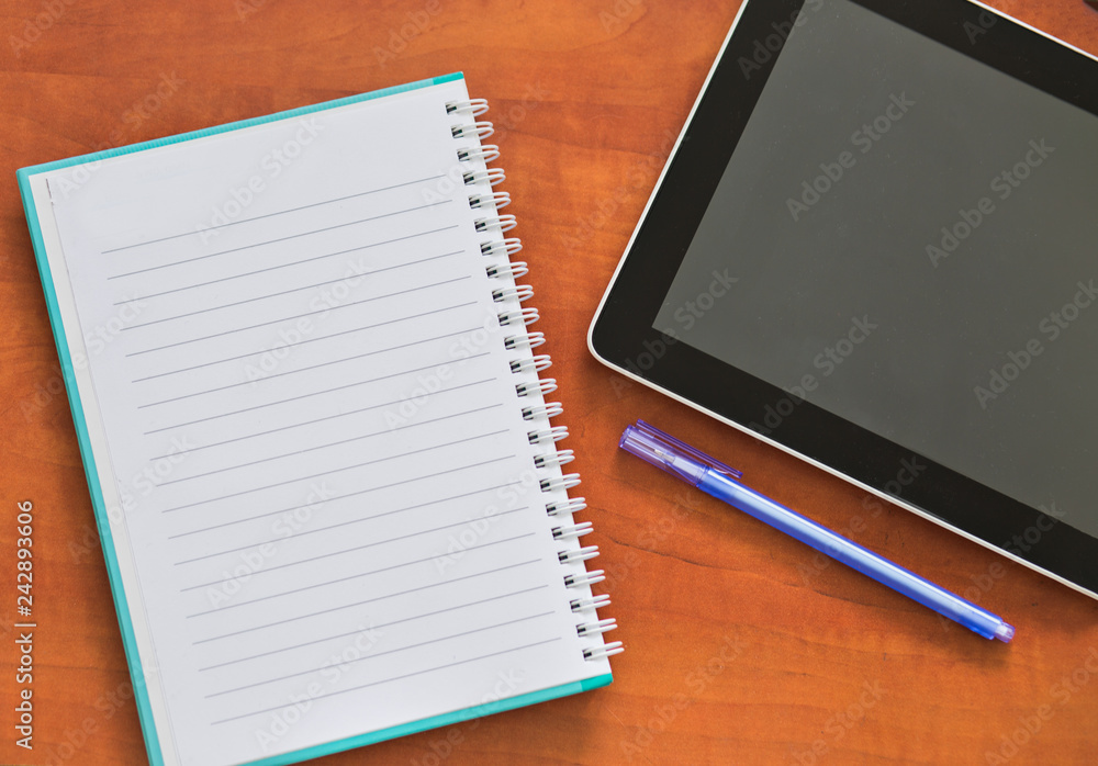 White notebook with pen and black tablet on wooden background. White notebook with pen and black tablet on wooden background.
