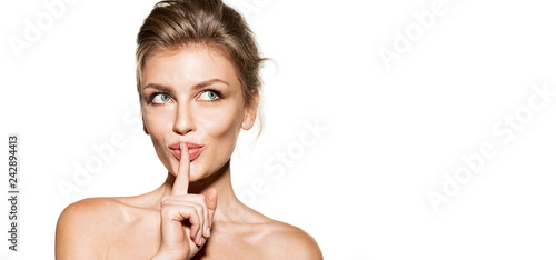 Portrait of charming young woman showing shhh sign. Beautiful blonde model with shiny skin and bare shoulders posing isolated on white background. Beauty and silence concept photo