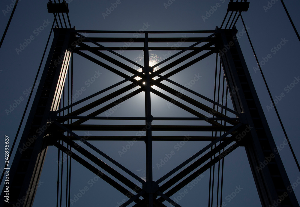 Silhouette of metal and cable bridge against the sun Silhouette of metal and cable bridge against the sun