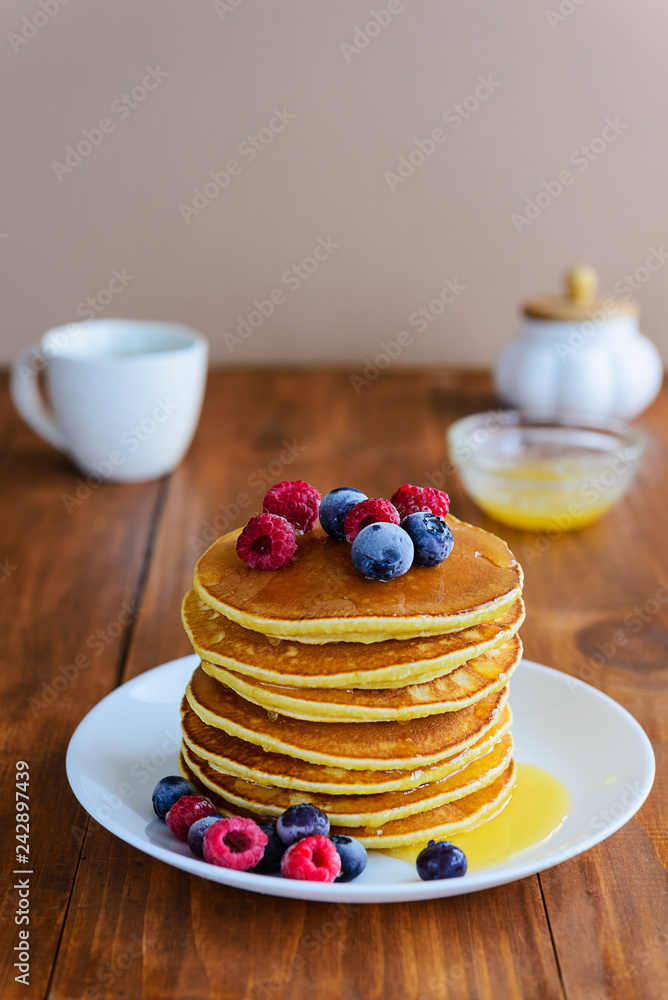 American pancakes with berries and honey on a wooden table American pancakes with berries and honey on a wooden table