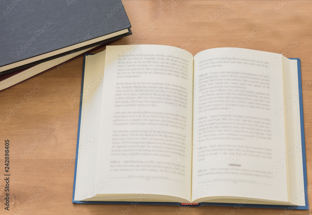 Fototapeta premium Open book with pile of closed books on wooden background.