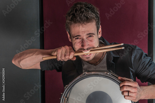 Young caucasian drummer with snare drum, biting his sticks
