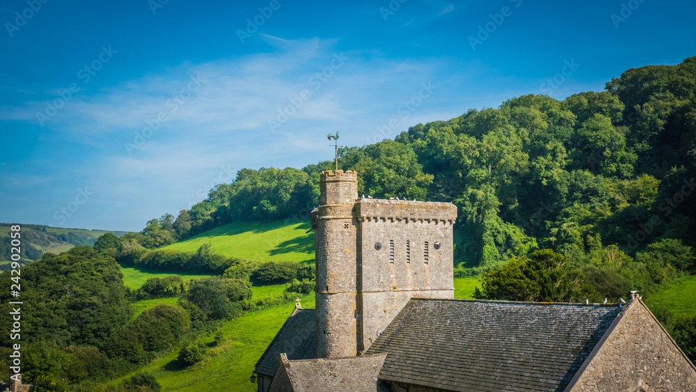 Old English norman, romanesque church, tower of a castle in a green hilly landscape on a summer sunny day with blue sky in the UK in a holiday Dorset countryside between Sidmouth and Lyme Regis. Old English norman, romanesque church, tower of a castle in a green hilly landscape on a summer sunny day with blue sky in the UK in a holiday Dorset countryside between Sidmouth and Lyme Regis.
