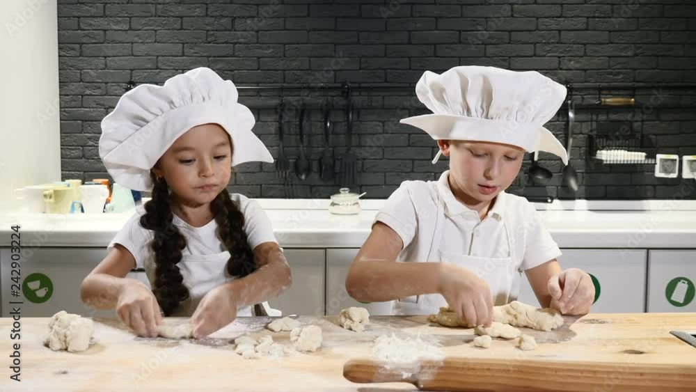 Two preschool kids working side by side cooking pies and cookies. Children chefs wear hats and aprons. 6-7 year old guys play chefs. 4k Two preschool kids working side by side cooking pies and cookies. Children chefs wear hats and aprons. 6-7 year old guys play chefs. 4k