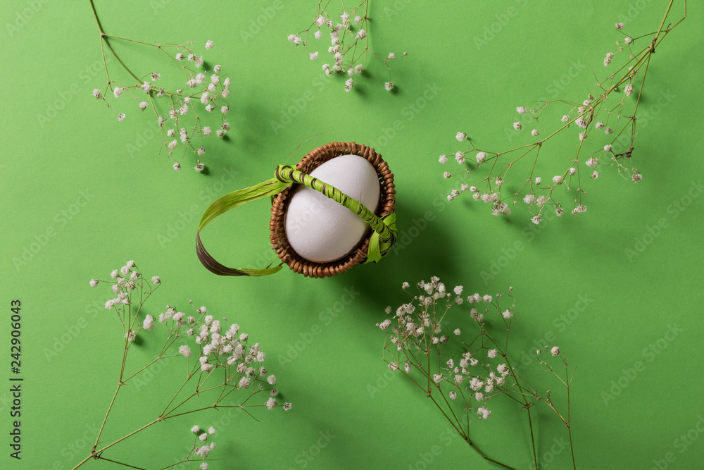 White egg in basket on green background with flowers