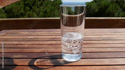Serving raki in a glass on a wooden table on a terrace with sea view.