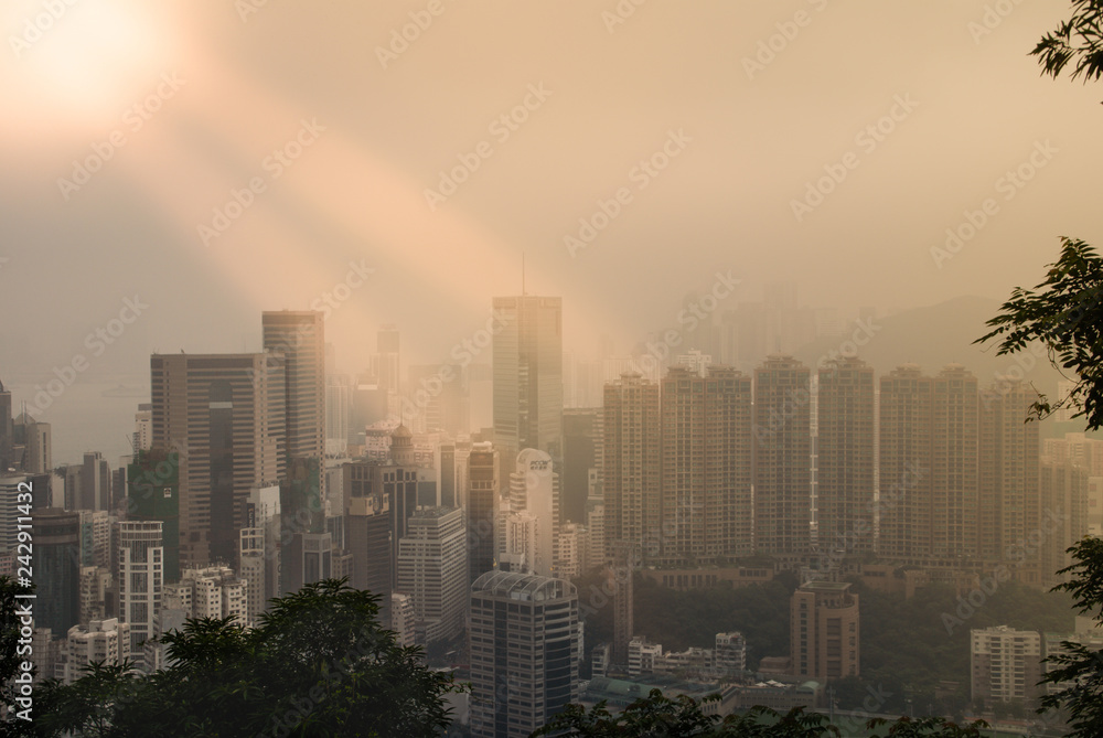 Hong Kong, China  - May 12, 2010: The highrise buildings of Hong Kong Island captured in fog, seen from halfway Victoria mountain. Isolated sun beams descending on parts.