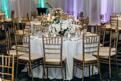 Wedding dinner table decor. Indian reception or banquet. Pastel and white colors. Long tables decorated with white flowers and golden cutlery. photo