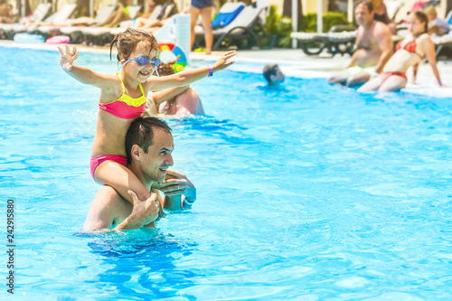 Little girl and happy dad having fun together in outdoors swimming pool