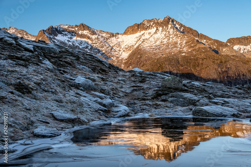 Mountain range lit with the evening light and reflecting in frozen pond photo