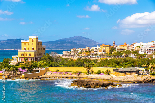 Mediterranean seacoast in Alghero city, Sardinia, Italy. Spring flowers and trees on foreground, colourful buildings of Alghero old city center on background photo
