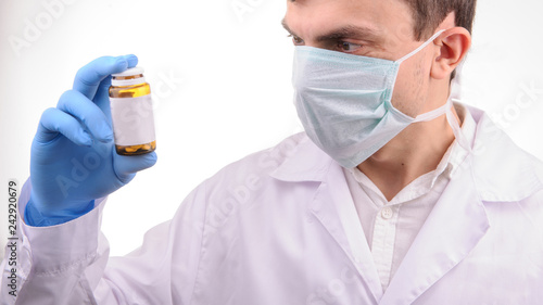a doctor with mask in a white uniform looking at a bottle with pills that he is holding in his hand in a blue glove