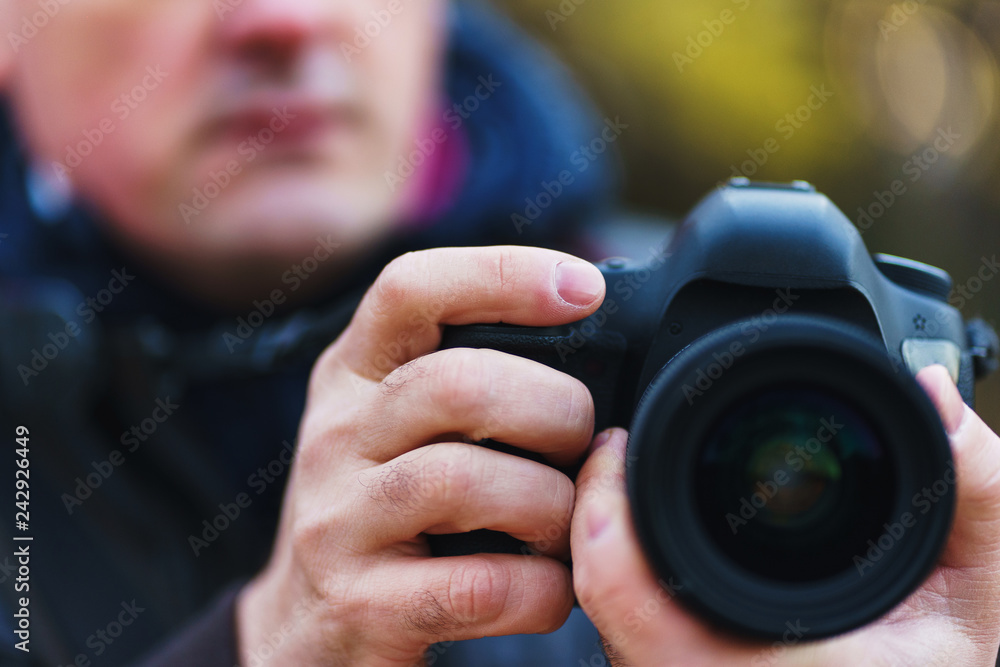 Male photographer is holding a large black SLR camera while photographing in the park. Male photographer is holding a large black SLR camera while photographing in the park.