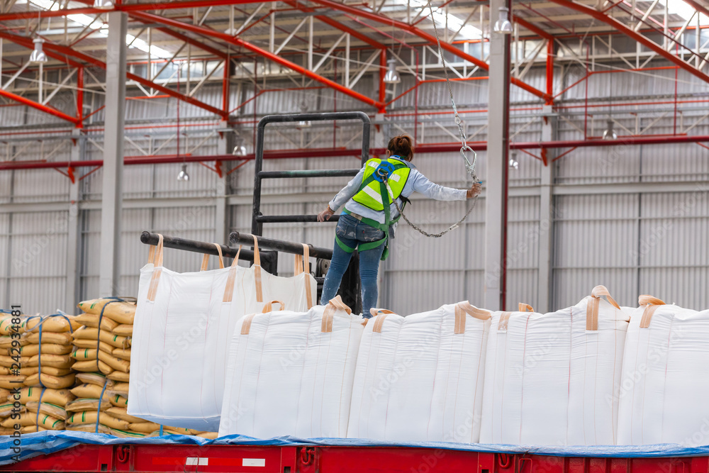 Construction worker wearing safety harness and safety line working on the truck of cargo in the warehouse for distribution ,import export business.