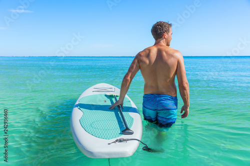 Stand up paddle boarding fitness man swimming in turquoise caribbean ocean water.