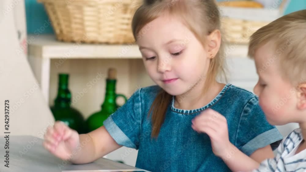 Tilt down of little brother and sister learning how to use digital tablet together at kitchen table in home