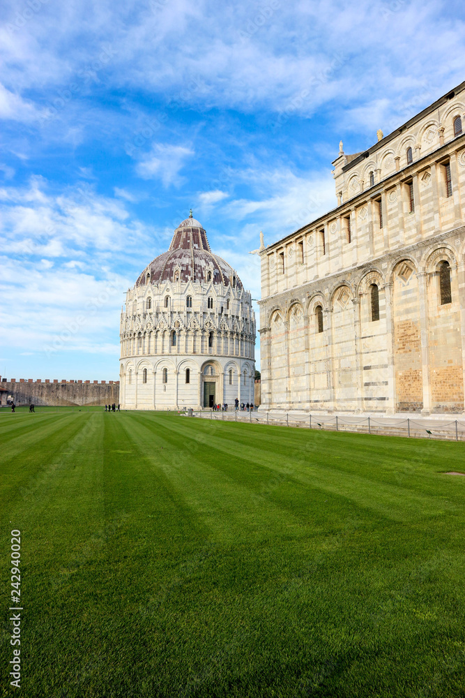 Green lawn at the piazza dei miracoli (square of miracles) with Pisa baptistery and cathedral, blue sky on the background, Tuscany, Italy