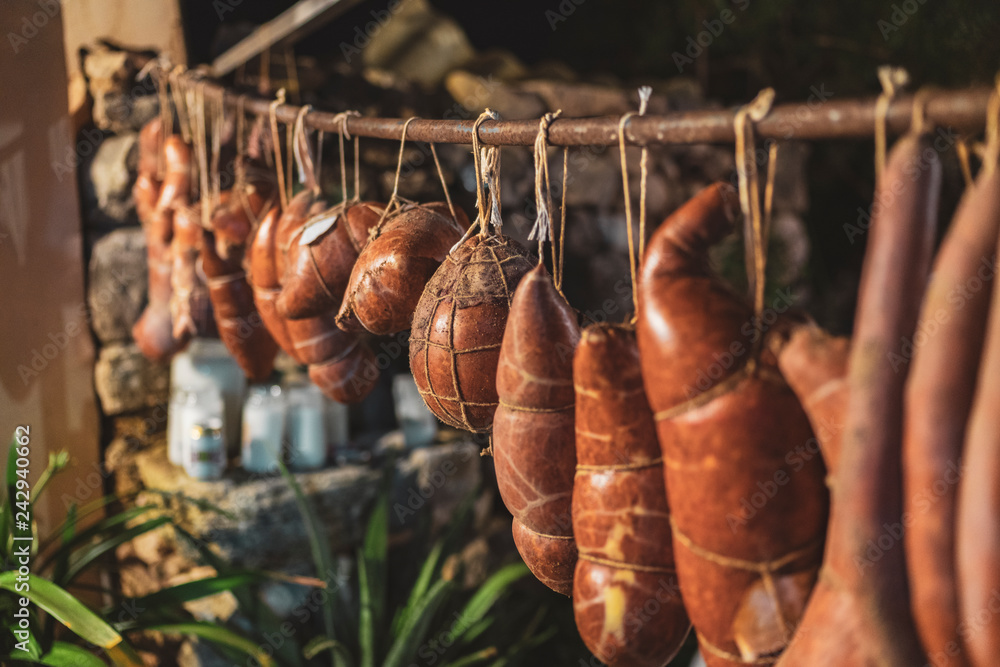 Sobrassadas hanging from a bar with jars of butter in the background