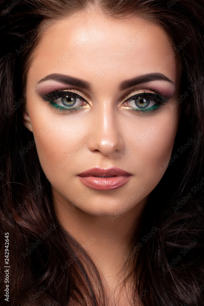 Portrait of young beautiful woman with evening make up posing over black background. Red and gold multicolored smokey eyes. Luxury skincare and modern fashion makeup concept. Studio shot.