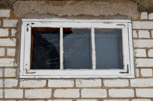 Old dirty white wooden window with broken glass pane on brick wall outdoors.