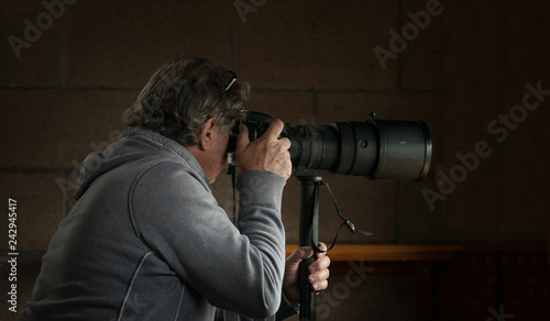 Older man, photographer, paparazzi holding digital camera and long, telephoto lens 