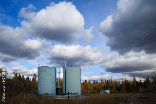 Blue bitumen tanks in a field under a clouded sky