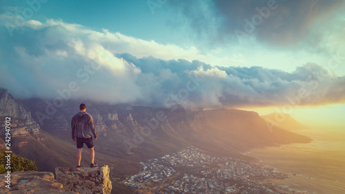 Young man standing on the edge at the top of Lion's head mountain in Cape Town with a beautiful sunset view