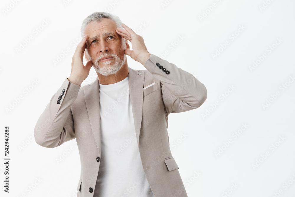 Portrait of old man having headache from bothering loud noise from neighbours living upstairs holding hands on head bending body and looking up with bothered and irritated expression Portrait of old man having headache from bothering loud noise from neighbours living upstairs holding hands on head bending body and looking up with bothered and irritated expression