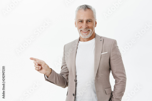 Grandfater inviting guests to look at fascinating colection. Elegant and self-assured good-looking wise old man in suit with grey beard and hair pointing left and smiling delighted at camera photo