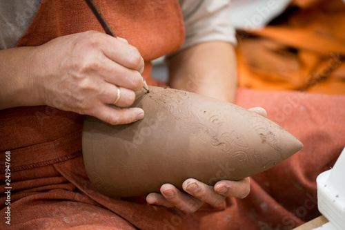 Ceramic workshop, the master puts otnament on unfired earthenware jug. Close-up of master hands. Made by hand, a hobby. Background illustrating the manual work with clay. photo