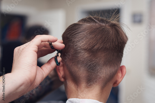 Barber making hairstyle to a Caucasian boy using scissors and hairbrush.