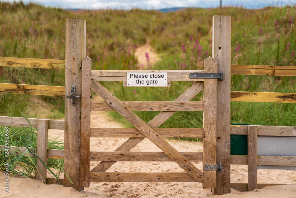 Sign: Please close the gate, seen on a closed gate in Ross Sands near Seahouses in Northumberland, England, UK