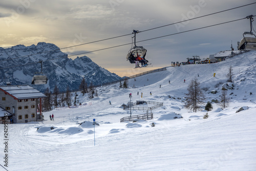 ski slopes with skiers and chairlift at sunset. Trentino, Italy